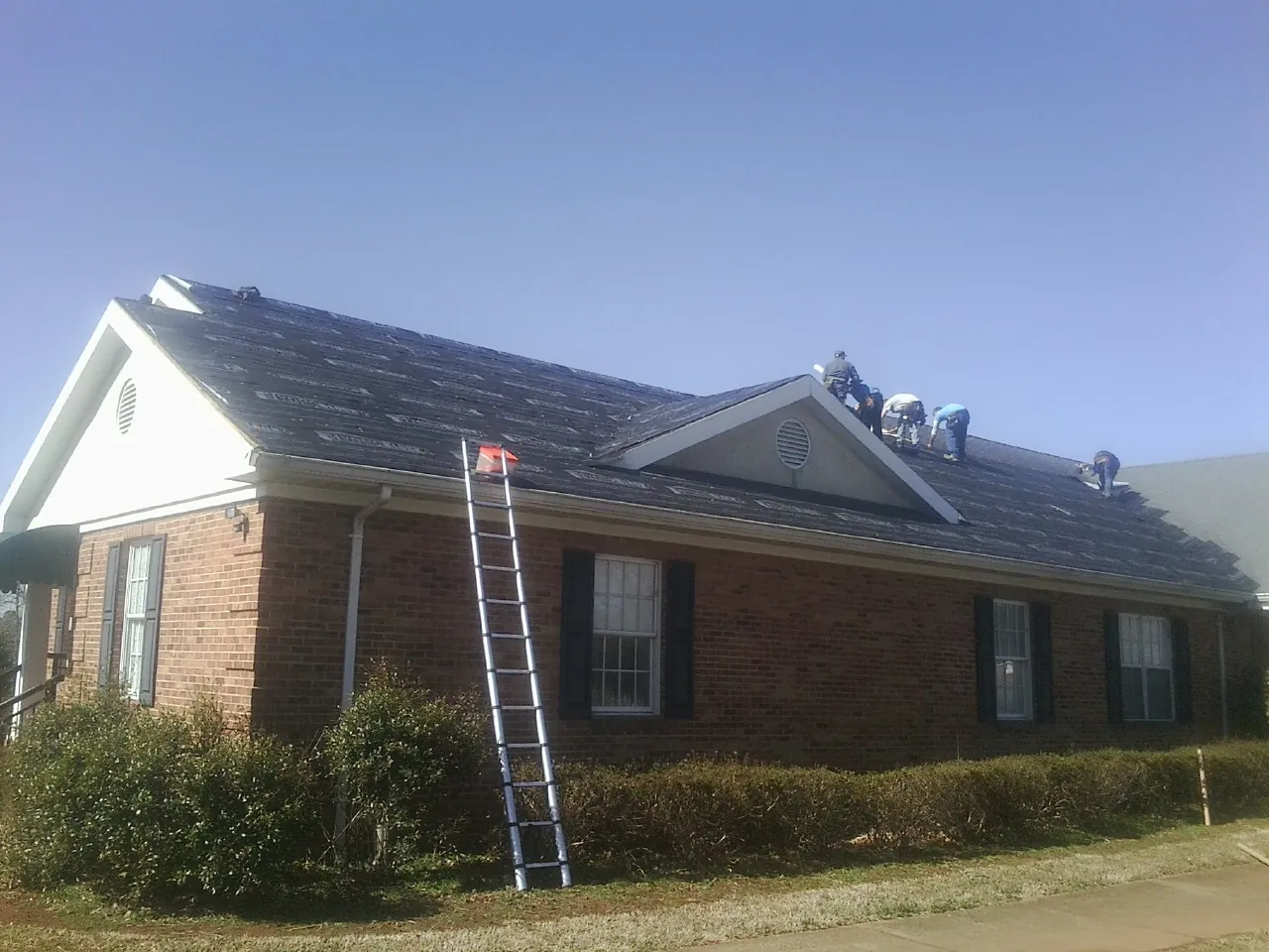 Crew tearing shingles off a brick ranch roof with a ladder set — Emergency Roof Repair work by our crew in Huntsville