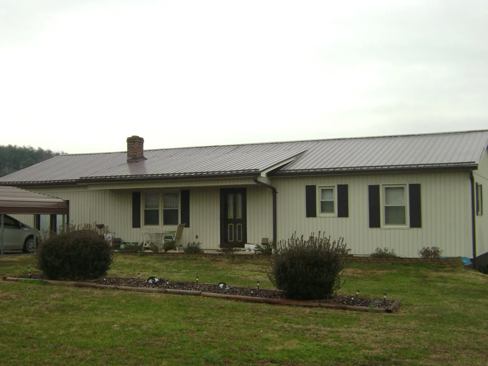 Brown metal roof on a cream sided ranch home with a brick chimney in Huntsville