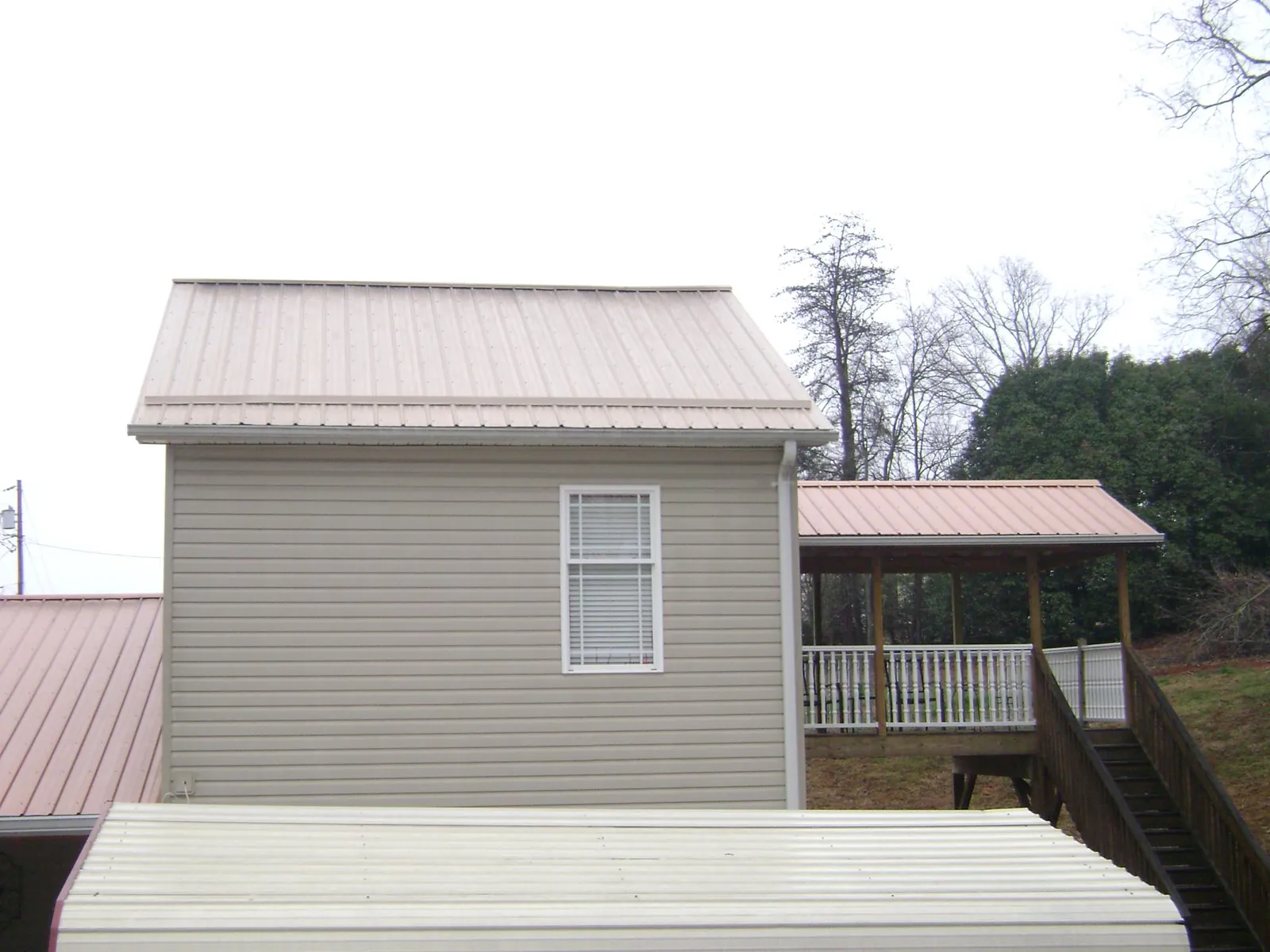 Tan metal roofs on a two story addition and attached porch, from a Roof Replacement job in Huntsville